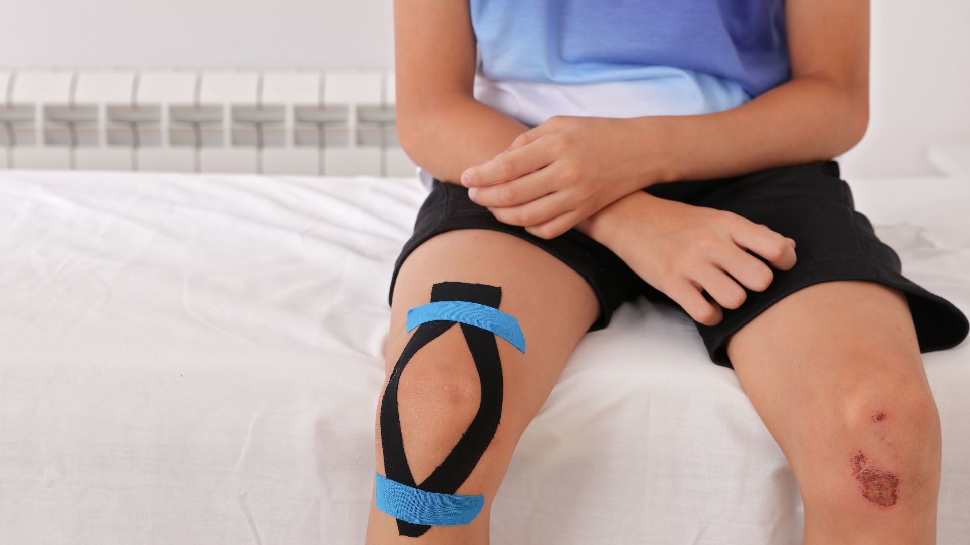 Παιδί με κινησιοταινία (kinesio tape) στο γόνατο, αποτυπώνοντας τη διαχείριση των διαταραχών μυϊκού τόνου.