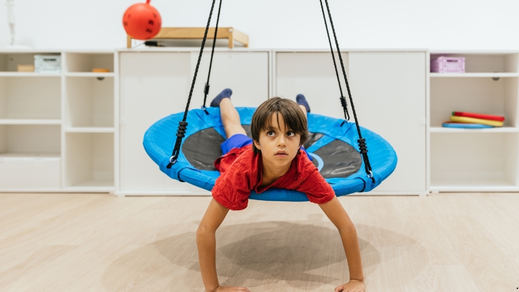 Παιδί συμμετέχει σε αισθητηριακή ολοκλήρωση σε αιώρα κατά τη διάρκεια συνεδρίας εργοθεραπείας.