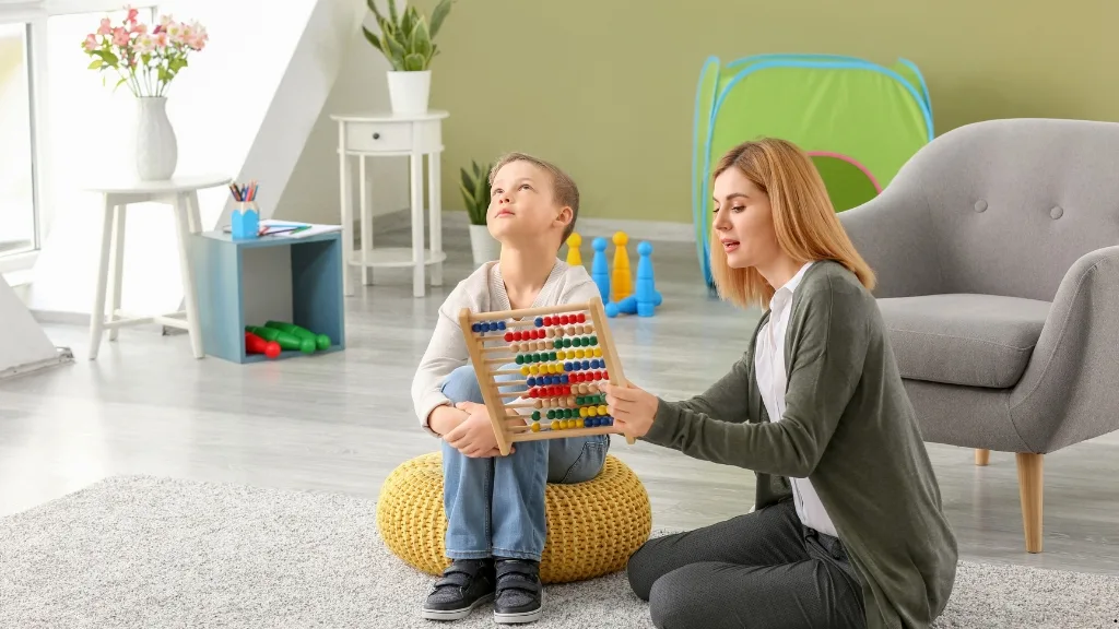 Παιδοψυχολόγος δείχνει έγχρωμο αριθμητήριο σε παιδί με δυσκολίες επικοινωνίας, σε ειδικά διαμορφωμένο θεραπευτικό χώρο.