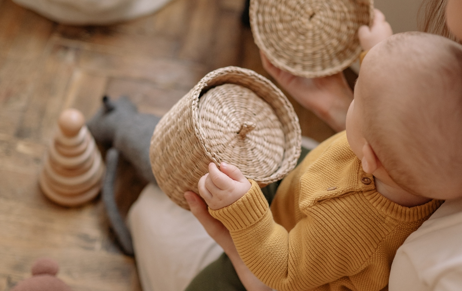 Μωρό παίζει με ξύλινα και υφασμάτινα αντικείμενα, εξερευνώντας υφές και σχήματα.