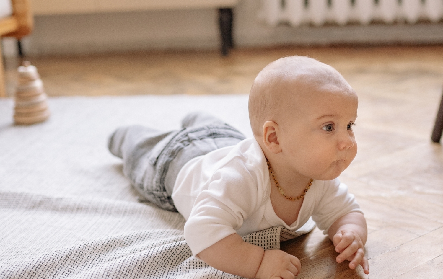 Μωρό ξαπλωμένο μπρούμυτα στο πάτωμα στηρίζεται στα χέρια, ενισχύοντας την κινητική ανάπτυξη.