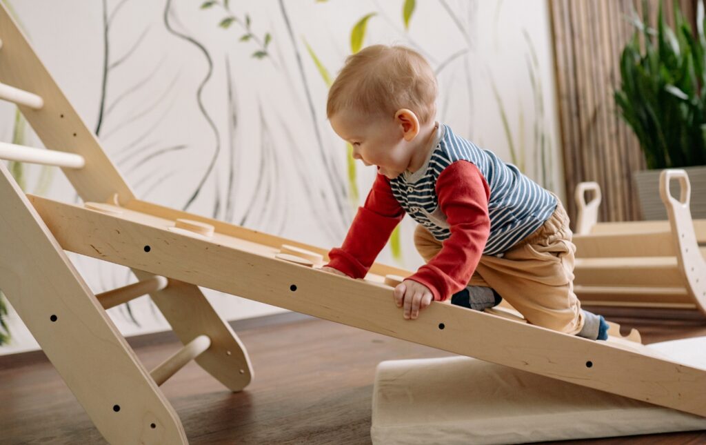 Μωρό σκαρφαλώνει σε ξύλινη κατασκευή παιχνιδιού, αναπτύσσοντας κινητικές δεξιότητες.